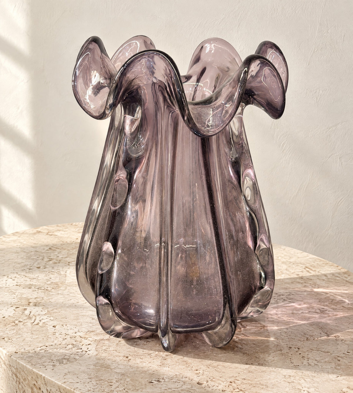 Big tapered smoky amethyst glass vase with a ruffled rim on a pale travertine table
