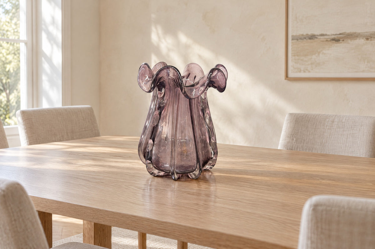 Big amethyst glass vase, empty, on a pale oak dining table in a light dining room