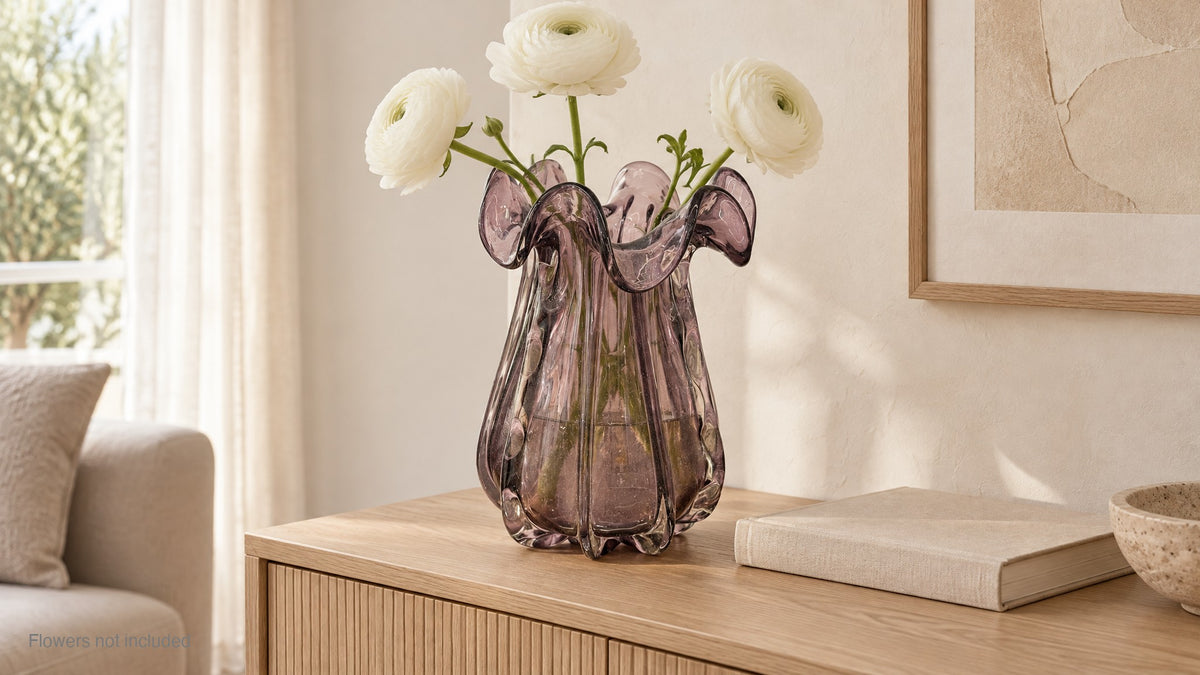 Big amethyst glass vase holding white ranunculus on a pale oak sideboard; flowers not included
