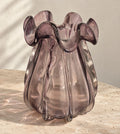 Small smoky amethyst glass vase with a ruffled rim on a pale travertine table