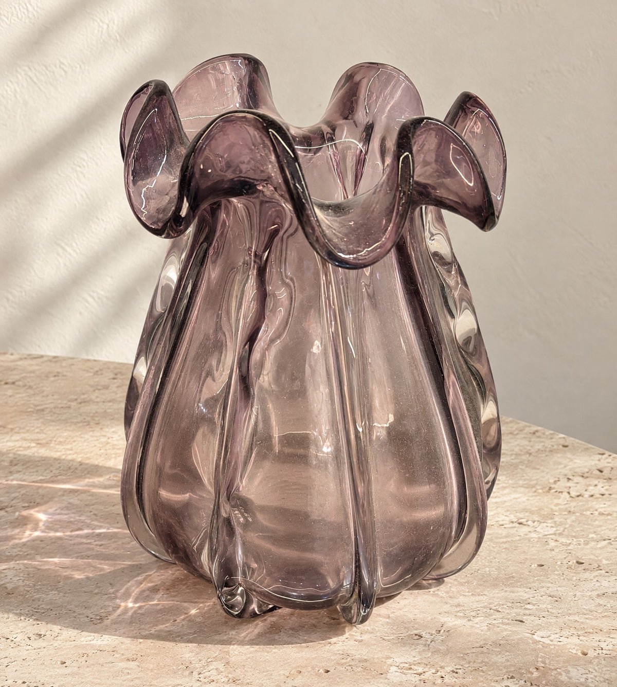 Small smoky amethyst glass vase with a ruffled rim on a pale travertine table