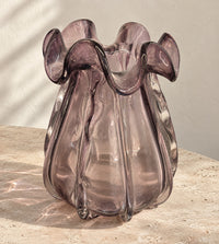 Small smoky amethyst glass vase with a ruffled rim on a pale travertine table