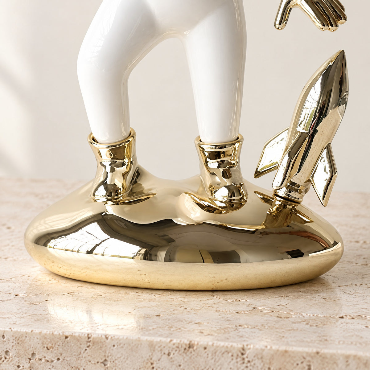 Close-up of the astronaut's gold-plated boots, small gold rocket and rounded gold base on travertine