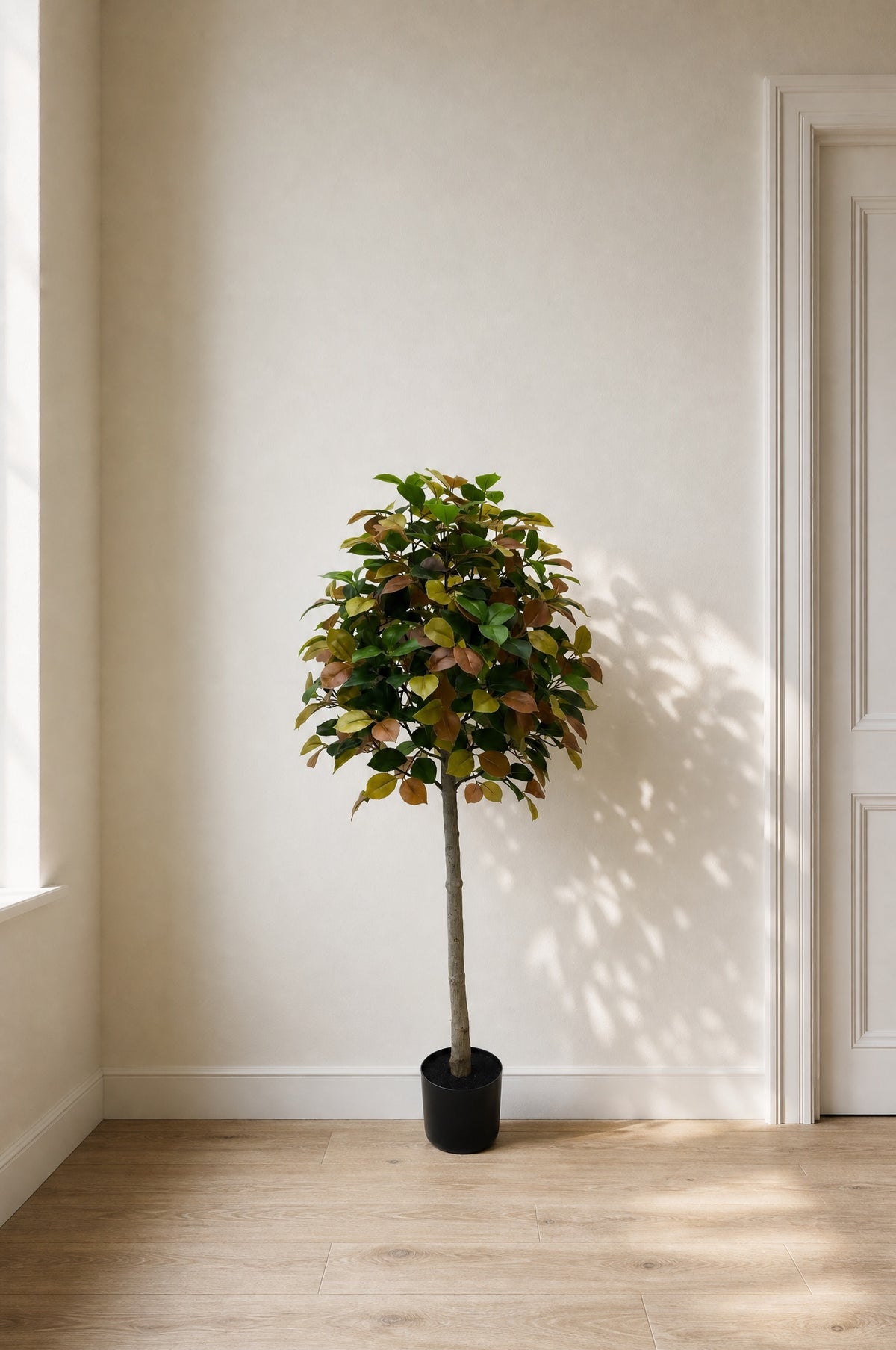 Autumn camellia artificial tree with green, gold and copper leaves in a black nursery pot in a quiet ivory corner