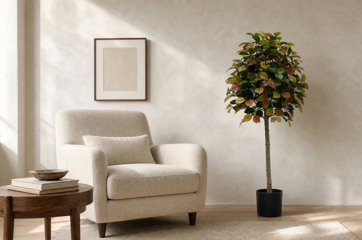 Autumn camellia artificial tree in its black nursery pot beside a linen armchair, showing its 130 cm height