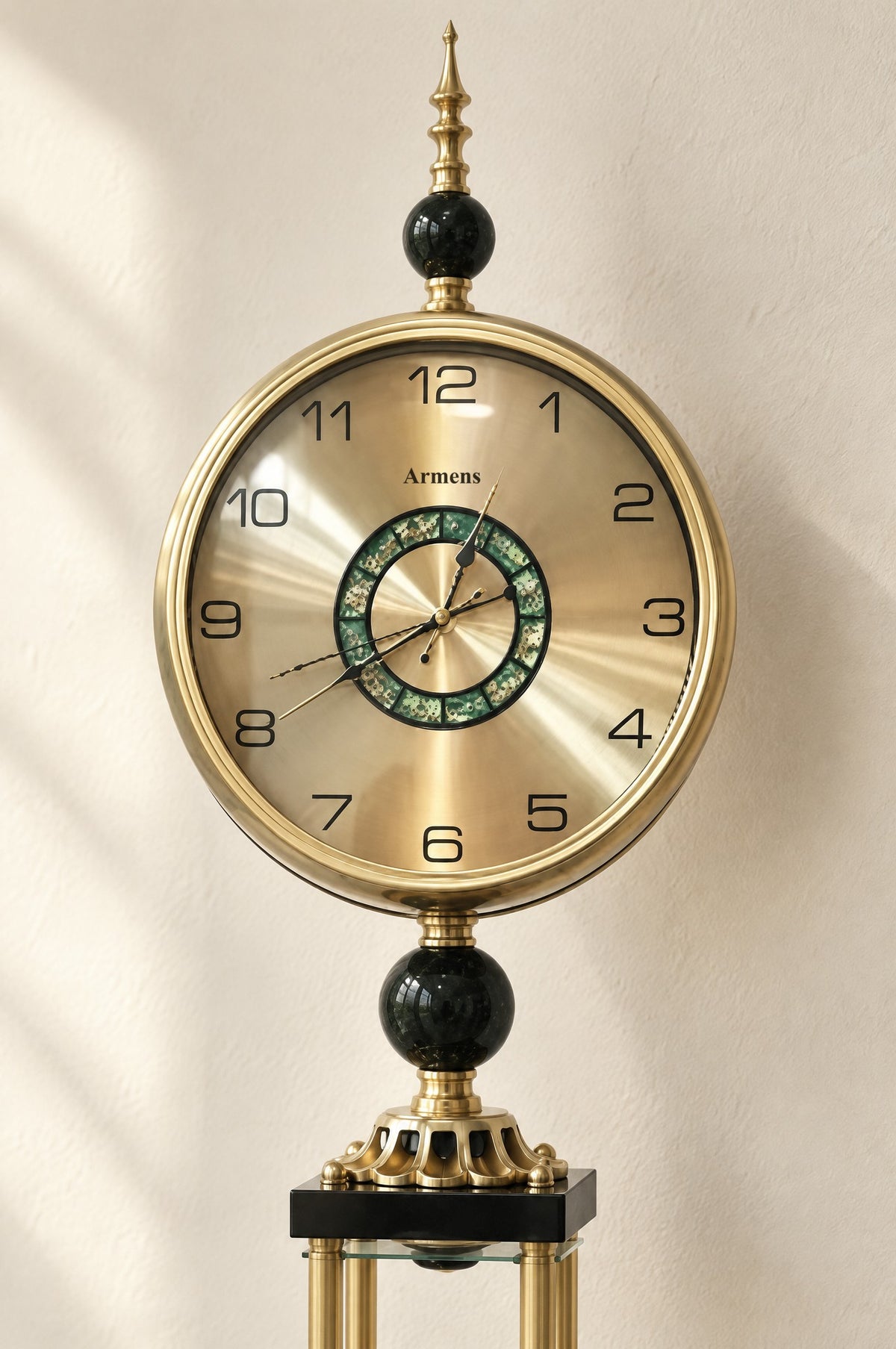 Close view of the clock head: gold dial behind glass with black Arabic numerals, the Armens name and an open-gear centre set in natural green mother-of-pearl
