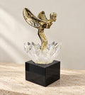 Gold winged metal figure rising from a K9 crystal lotus on a black glass base, on a travertine console