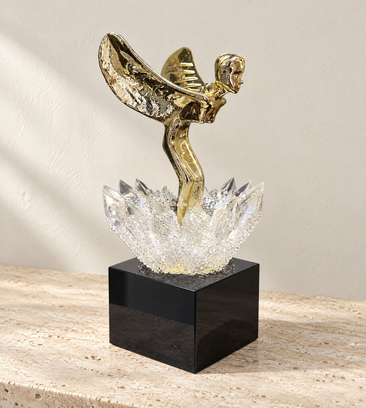 Gold winged metal figure rising from a K9 crystal lotus on a black glass base, on a travertine console