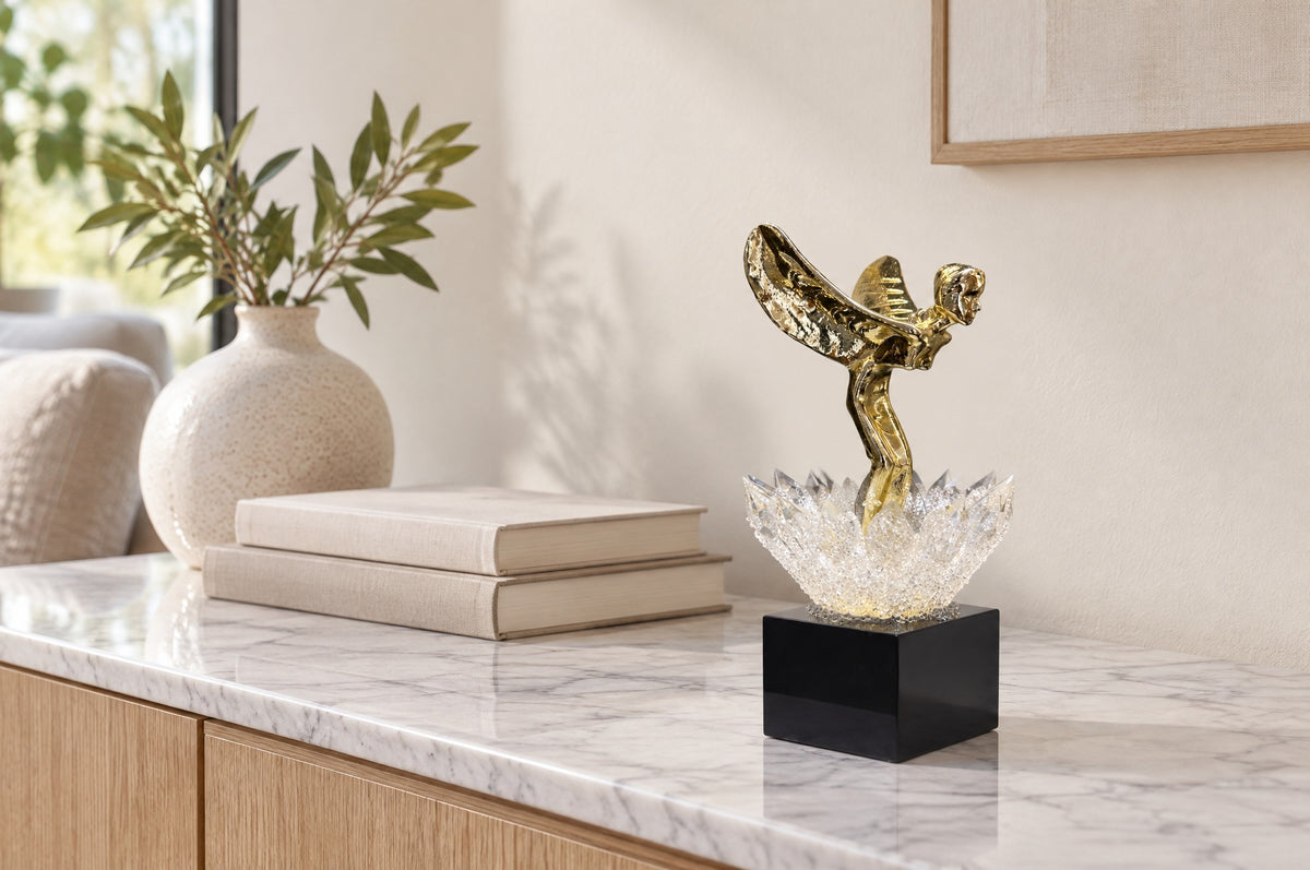 Crystal lotus sculpture with gold winged figure on a white marble console beside books and a ceramic vase