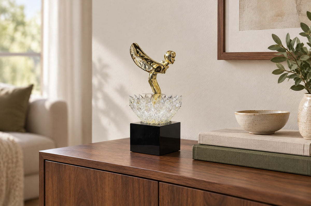 Crystal lotus sculpture with gold winged figure on a walnut console beside books