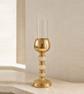 Gold-finish hurricane candle holder with three onyx spheres in the stem and a clear glass shade, on a travertine console