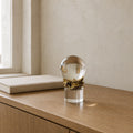 Clear K9 crystal sphere in a gold-finish metal cradle on a crystal column, standing on a light walnut console