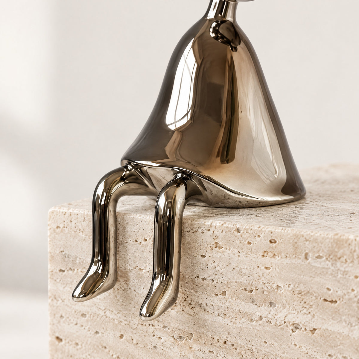 Gunmetal shelf-sitter with thin legs hanging over the edge of a travertine block