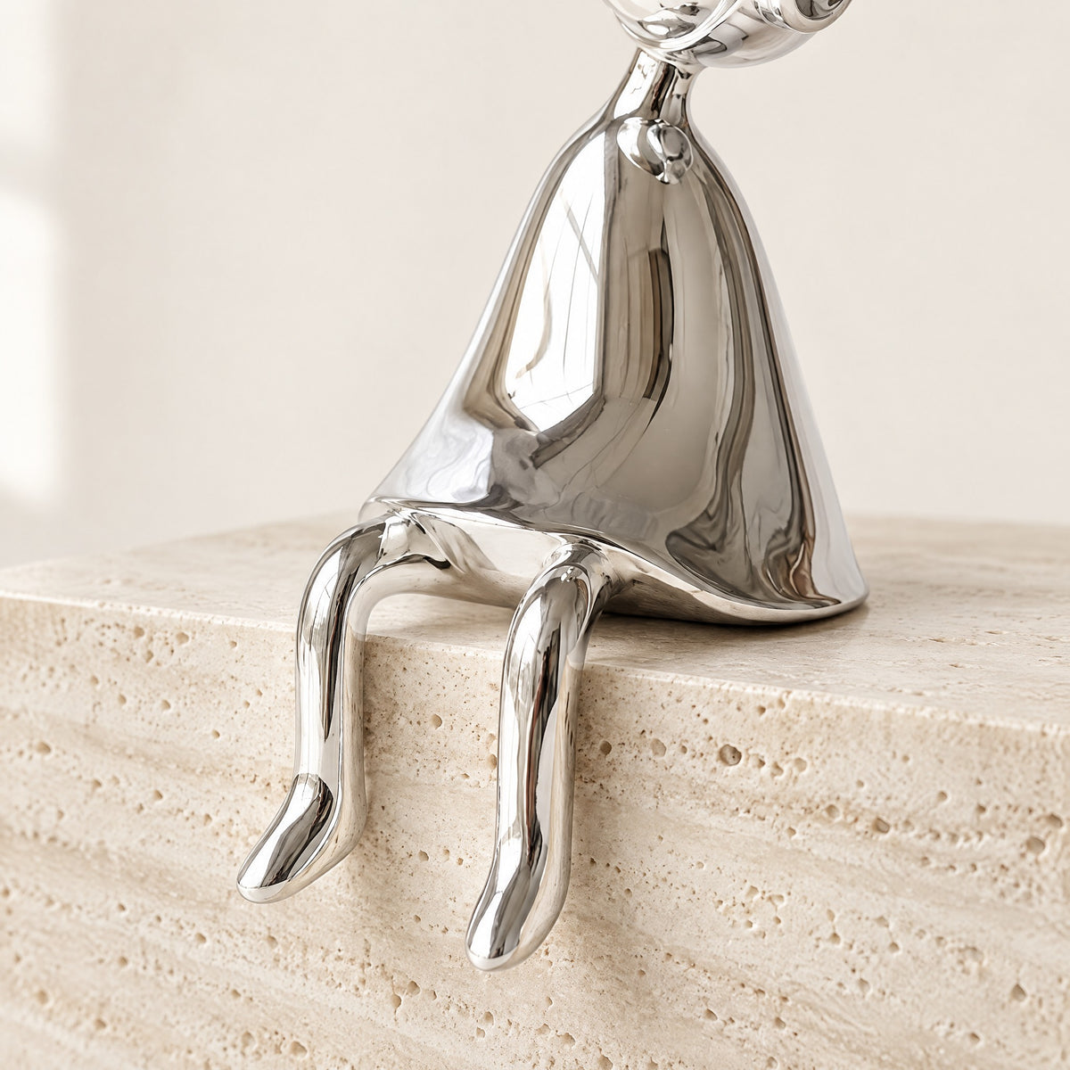 Silver chrome shelf-sitter with thin legs hanging over the edge of a travertine block