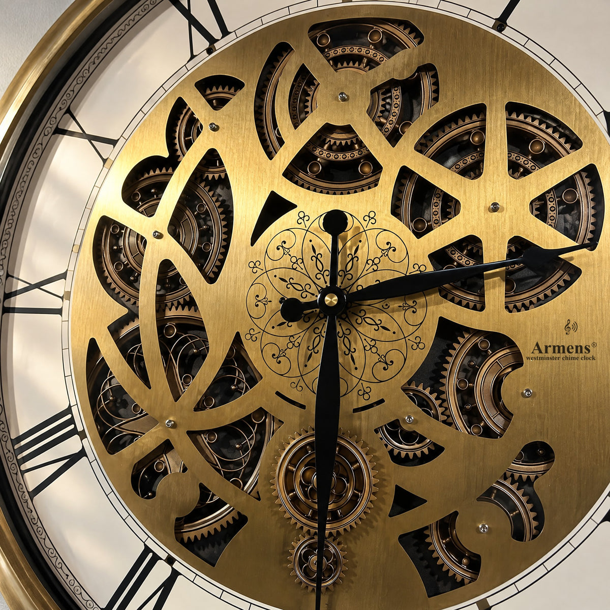 Close-up of the Golden Kinetic wall clock: laser-cut gold plate, gears behind it, engraved filigree rosette and the Armens mark