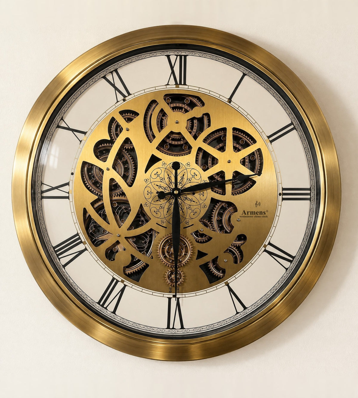 Golden Kinetic wall clock in a brushed gold steel frame with a laser-cut gold gear plate, black Roman numerals and the Armens westminster chime mark, front view