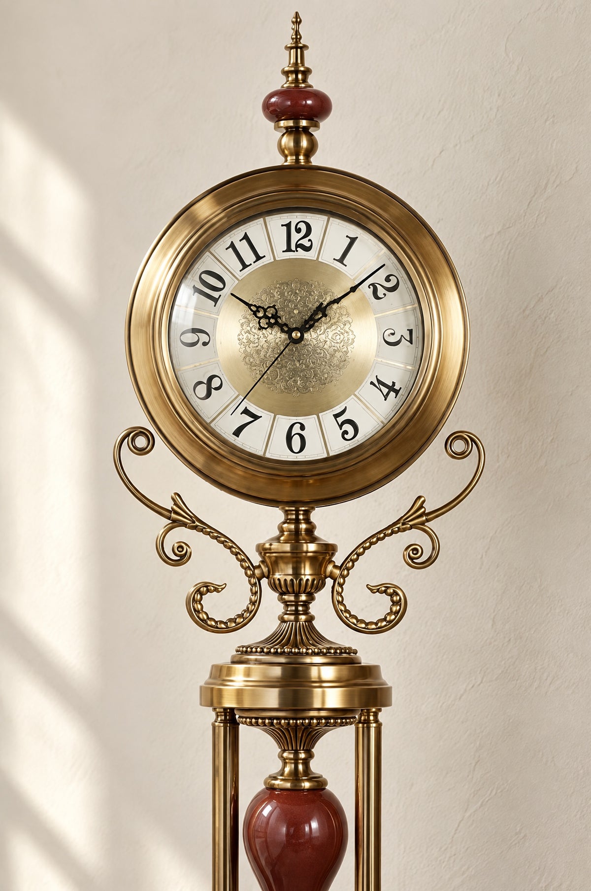 Close view of the clock head: ivory dial with black Arabic numerals behind glass, brass bezel, red ceramic finial bead and scrolled brass arms