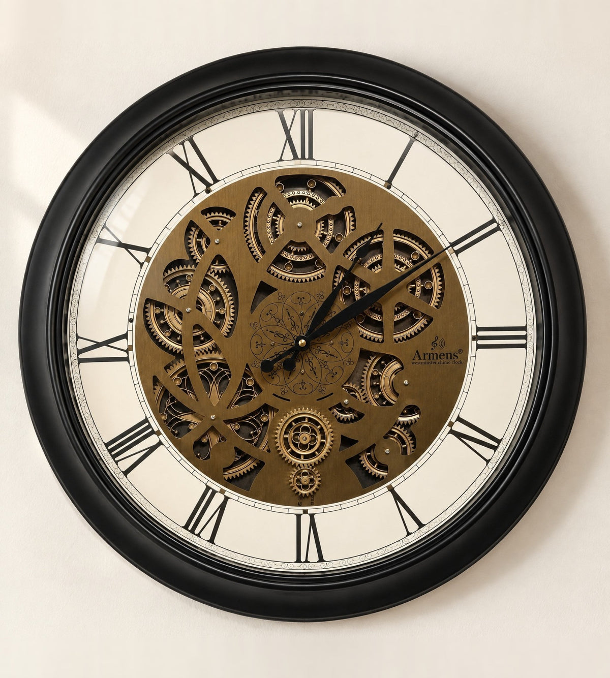 Obsidian Gear wall clock in a matte black steel frame with a laser-cut bronze-gold gear plate and black Roman numerals, front view