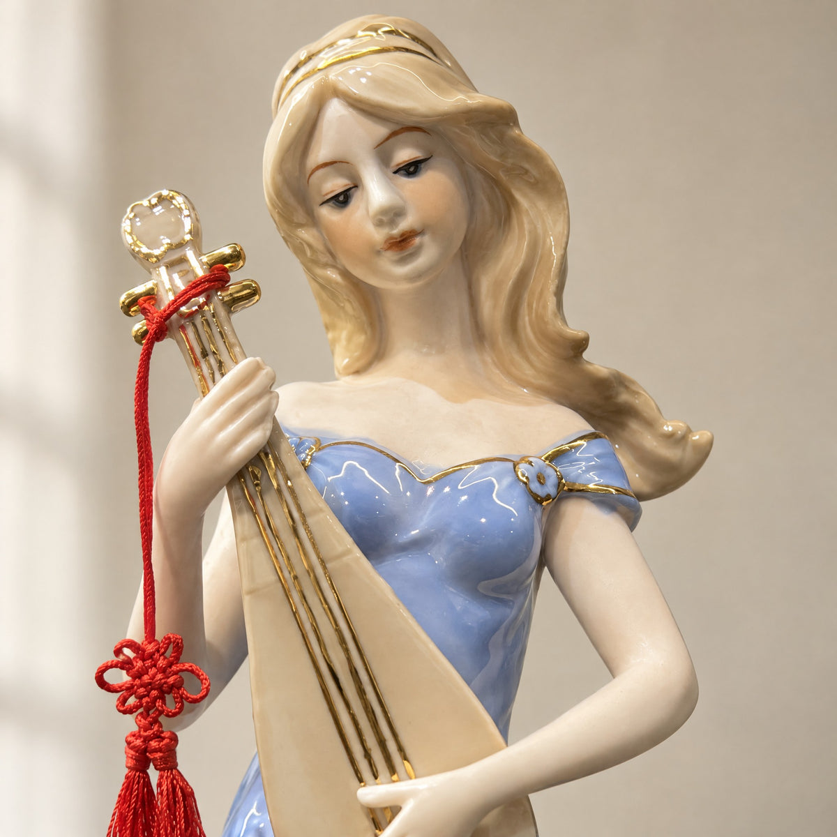 Close-up of the porcelain figurine's face, gold neckline and pipa with a red knotted cord and tassel