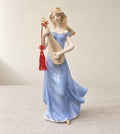 Serenade of Grace porcelain figurine in a periwinkle-blue gown with gold trim, playing a pipa with a red tassel, on linen against an ivory wall