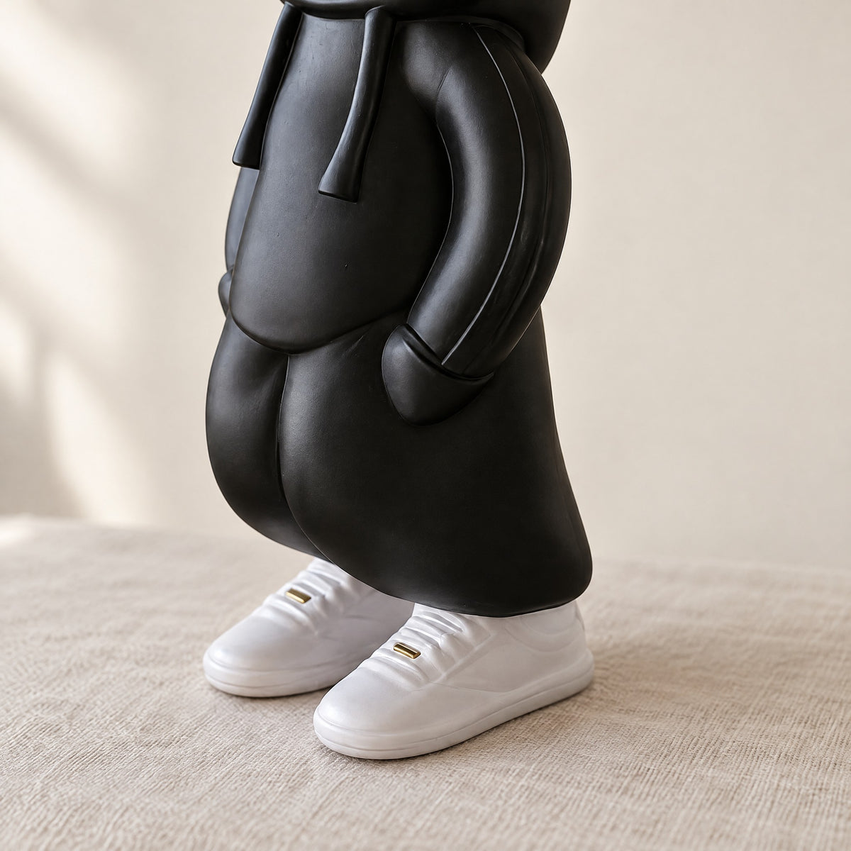 Close-up of the matte black hoodie, hands in pockets, and chunky white sneakers of the resin sculpture