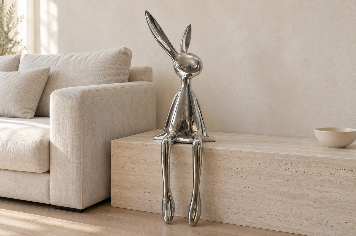 Chrome bunny sculpture on a low travertine bench beside a linen sofa in a light living room
