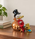 Chrome resin figurine of a duck in a top hat reclining on a rose-gold money bag, on a walnut desk beside two books