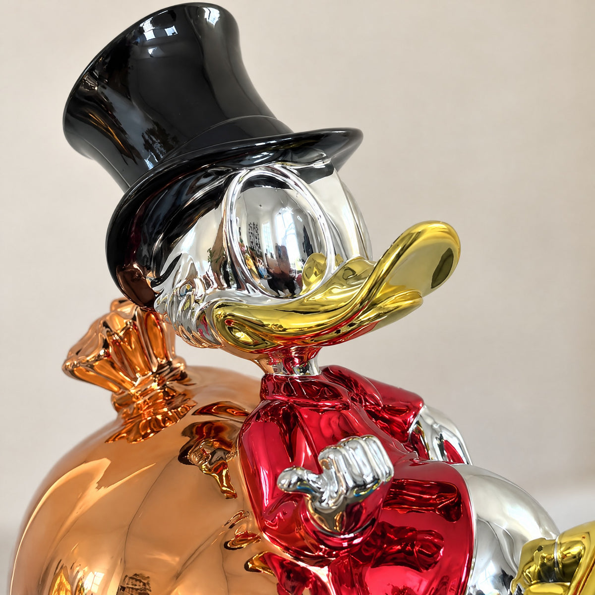 Close-up of the chrome duck figurine's black top hat, silver face, gold beak and red coat against the rose-gold money bag