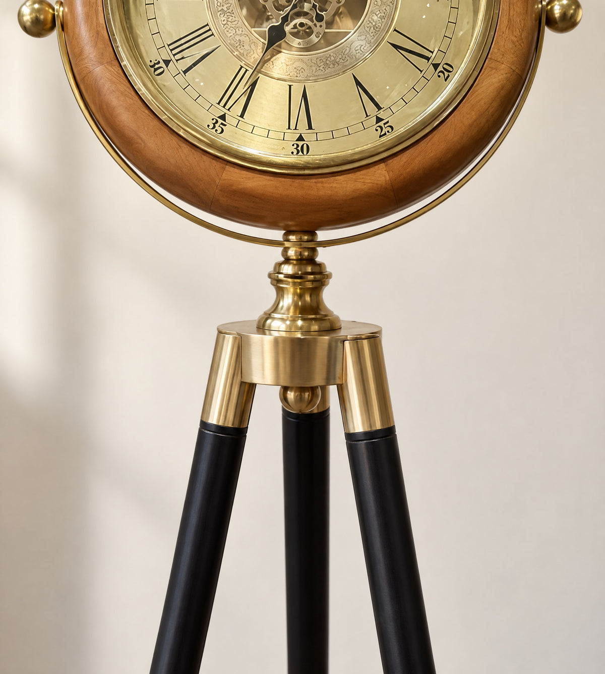 Close-up of the brass joint where the clock head meets the black tripod legs